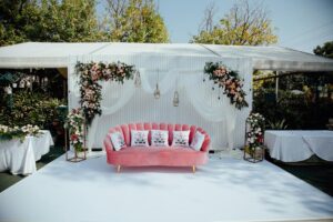 Outdoor wedding setup with floral arrangements, pink sofa, and elegant decor in Gurugram, India.